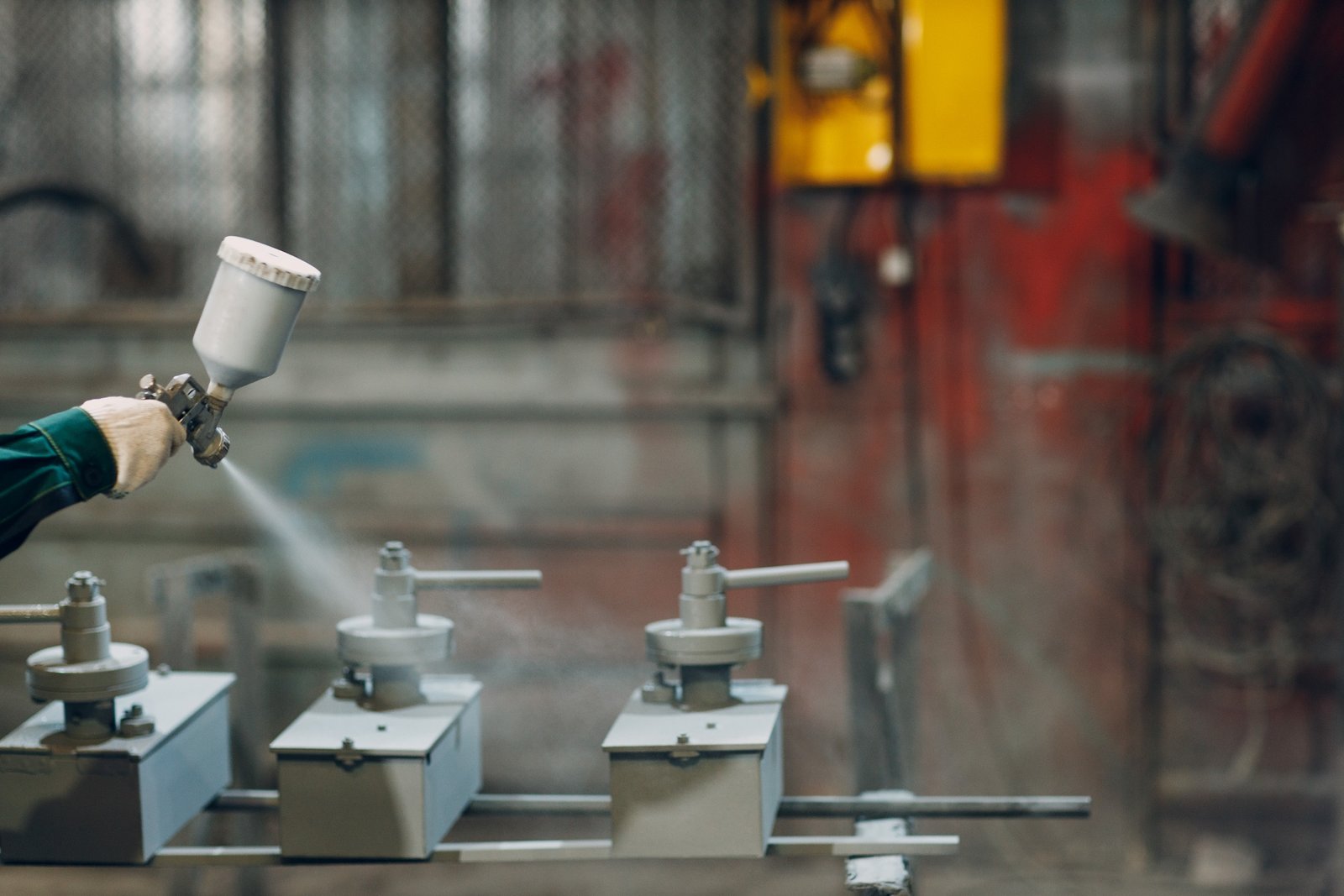 Powder paint coating of metal parts. Worker man in a protective suit sprays powder paint from gun on metal product construction at factory plant.