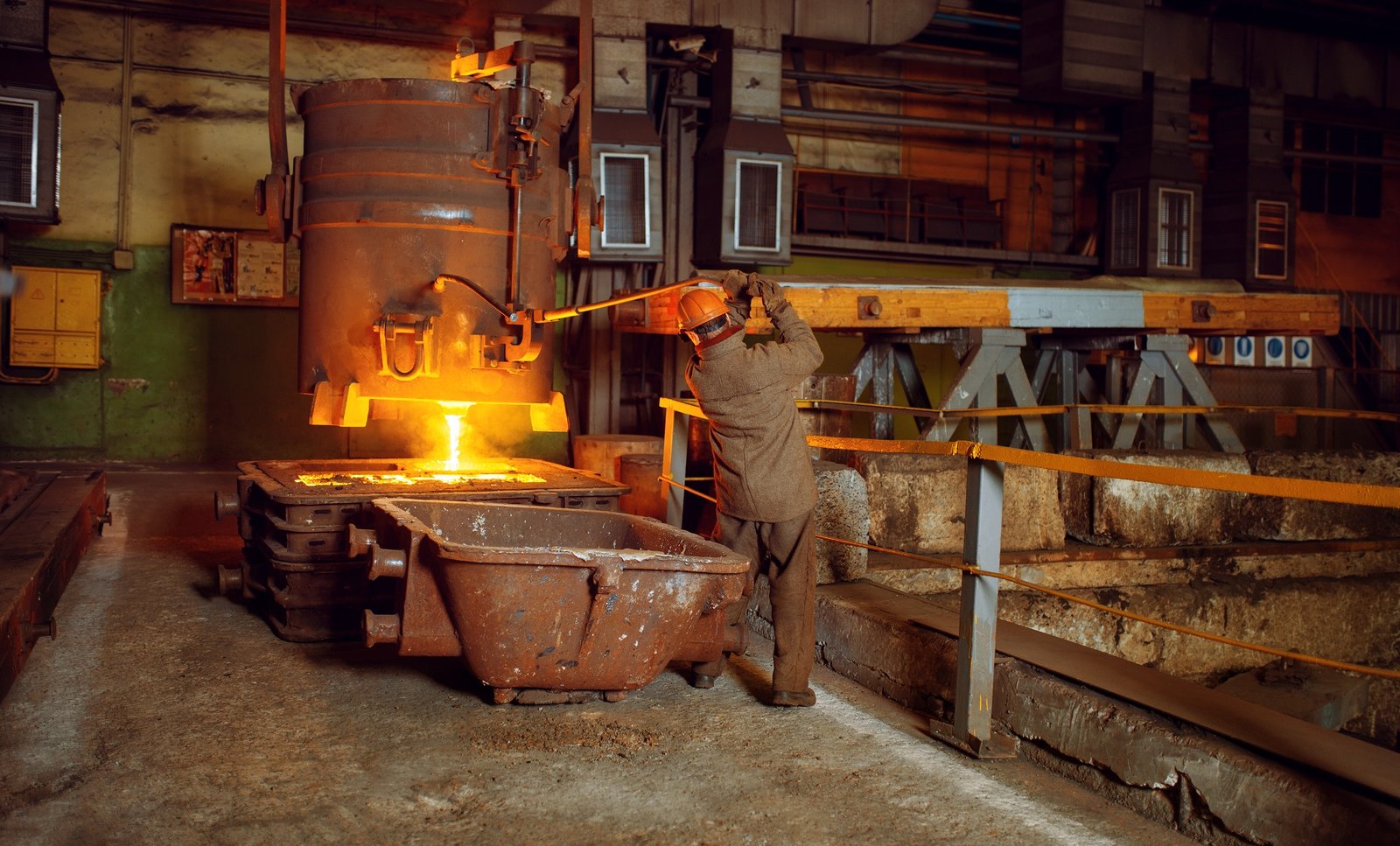 Steelmaker in helmet pours liquid metal from basket, steel factory, metallurgical or metalworking industry, industrial manufacturing of iron production on mill